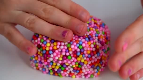 Руки дівчини, що грає зі слизом з різнокольоровими кульками на білому столі . — стокове відео