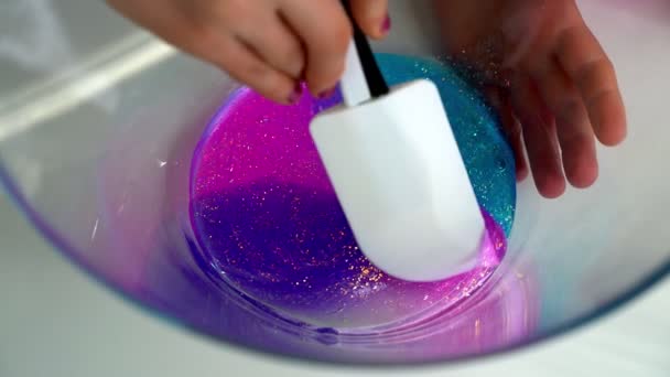 Hands of a girl stir multicolored slime sequins in a bowl on a white table. — Stock Video