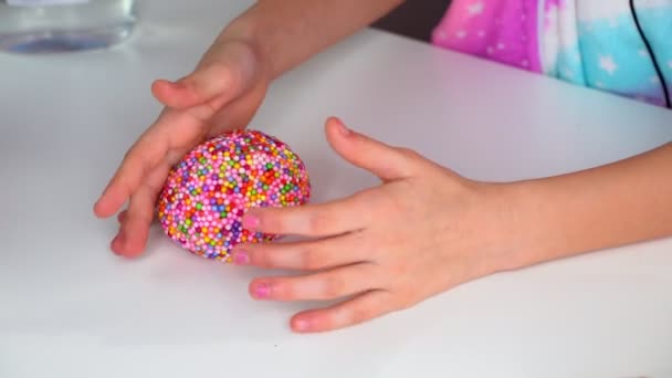 Hände eines Mädchens, das mit einem Schleim mit bunten Kugeln auf einem weißen Tisch spielt. — Stockvideo