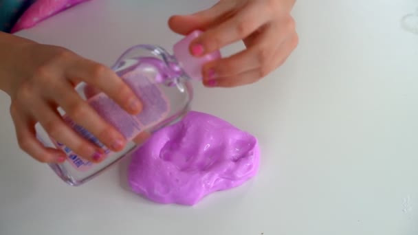 女の子の手は白いテーブルの上でピンクのスライムで遊ぶ。スリムに白い粘土を使用 — ストック動画