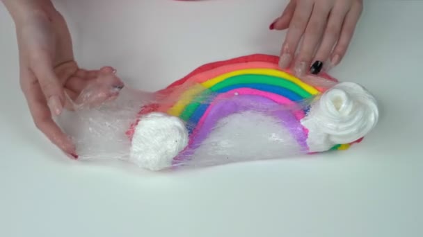 Hände eines Mädchens, die einen Regenbogenschleim auf einem weißen Tisch machen. — Stockvideo