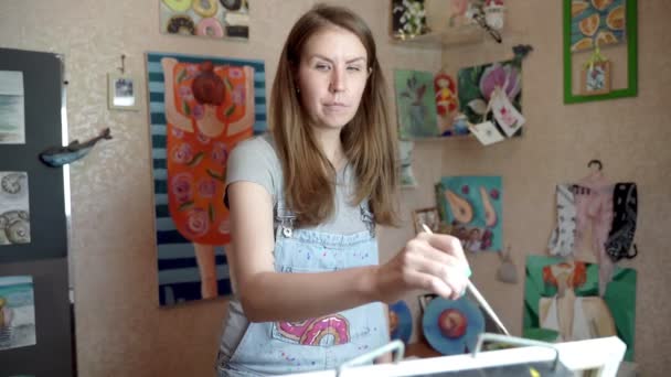 Κορίτσι καλλιτέχνης σε ένα μικρό δωμάτιο ζωγραφίζει μια εικόνα. — Αρχείο Βίντεο