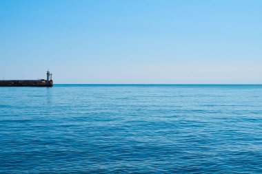 Deniz ve gökyüzünün arka planında deniz feneri, deniz tamamen sakin ve berrak bir gökyüzü, bahar. Deniz feneri, deniz ve iskele..
