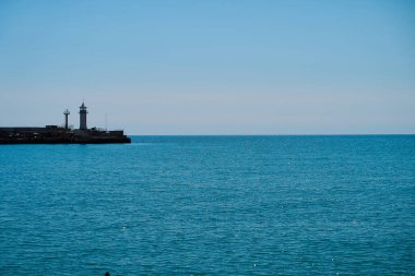 Deniz ve gökyüzünün arka planında deniz feneri, deniz tamamen sakin ve berrak bir gökyüzü, bahar. Deniz feneri, deniz ve iskele..