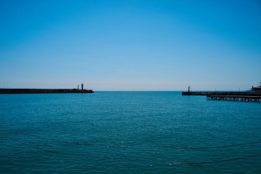 Deniz ve gökyüzünün arka planında deniz feneri, deniz tamamen sakin ve berrak bir gökyüzü, bahar. Deniz feneri, deniz ve iskele..