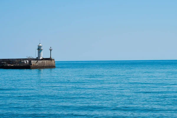 Lighthouse on the background of the sea and the sky, the sea is full calm and clear clear sky, spring. Lighthouse, sea and pier.