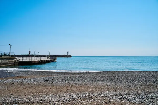 Deniz ve gökyüzünün arka planında deniz feneri, deniz tamamen sakin ve berrak bir gökyüzü, bahar. Deniz feneri, deniz ve iskele..