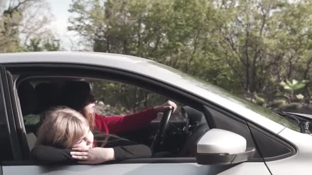 Familia en el coche. Mamá y su hija montan en un coche en un fondo de la naturaleza, una niña se encuentra pensativamente en la ventana de un coche y mira a la carretera . — Vídeo de stock