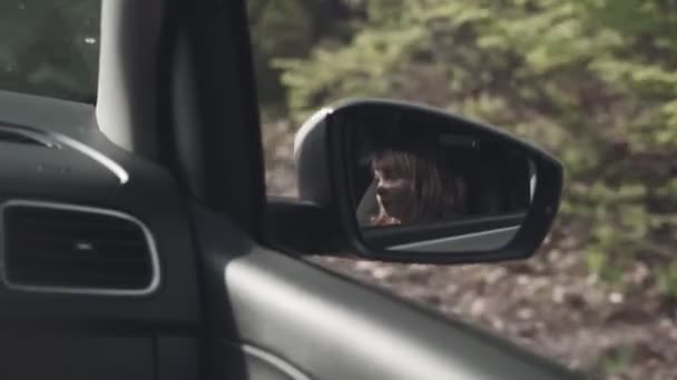 Család a kocsiban. Egy kislány tükörképe az autó oldalsó tükrében.. — Stock videók