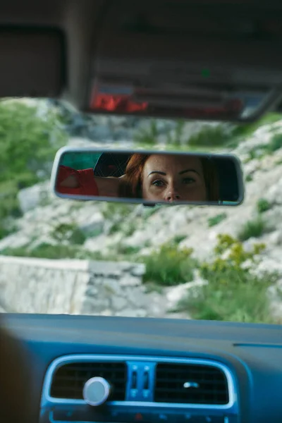 A young girl in a car looks at herself in the mirror, beautiful pensive eyes.