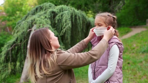 Una joven madre cuida a su hija con una máscara médica protectora . — Vídeos de Stock