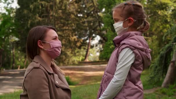 Молодая мать целует дочь в защитной медицинской маске, дочь целует в ответ — стоковое видео