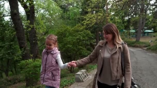 Maman et fille marchent au printemps dans le parc, marchent le long de la route et parlent entre eux . — Video