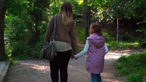 Mãe e filha caminham na primavera no parque, caminham pela estrada e conversam entre si . — Vídeo de Stock