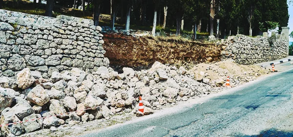 Yol boyunca destekleyen duvarın onarımı. Yoldaki yıkık dökük taş bir duvarın çitli parçası..