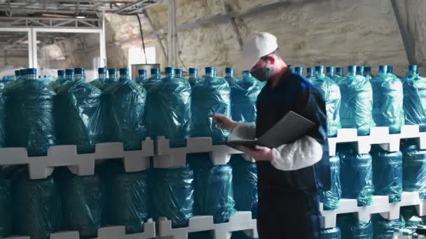 纯净水植物 这家工厂的一名穿着特别制服的雇员用装有清洁饮用水的大瓶子检查成品 然后提出报告并提交给另一名雇员 — 图库视频影像