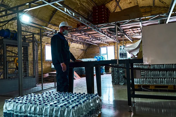 Pure drinking water plant. Work conveyor in the enterprise. A worker receives and arranges packaged bottles of water.