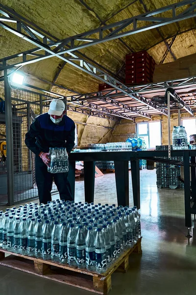 Pure drinking water plant. Work conveyor in the enterprise. A worker receives and arranges packaged bottles of water.