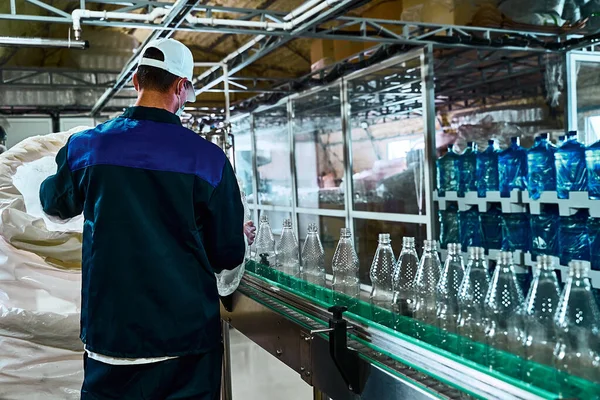 Pure drinking water plant. Work conveyor in the enterprise. A worker places liter bottles on a conveyor