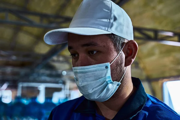 Koruyucu tıbbi maskeli bir işçinin portresi ve taşıyıcının arkasında beyaz bir şapka var..