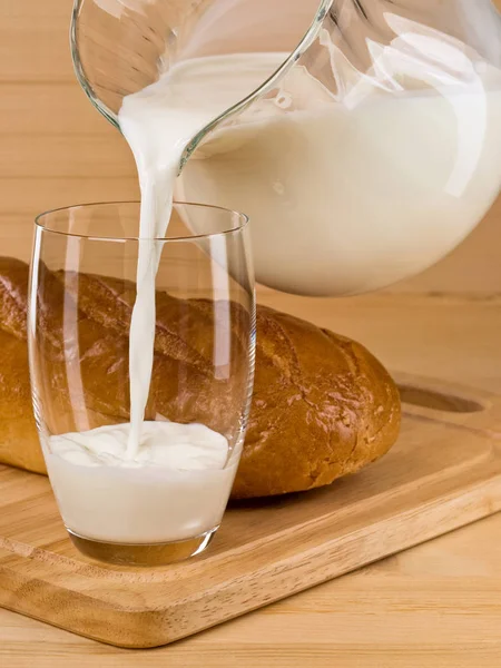 Наполнение стакана молоком из стеклянного кувшина — стоковое фото