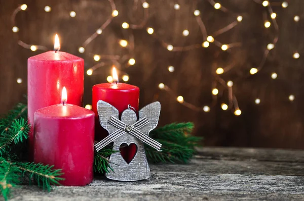 Rode kaarsen en decoratieve engel voor Kerstmis en Nieuwjaar op retro houten tafel en slinger verlichting achtergrond. — Stockfoto