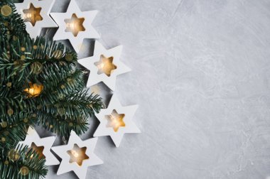 Sihirli Noel teması: rahat, sıcak ışıklar, çelenk, yıldızlar ve gri arkaplanda köknar dalları.