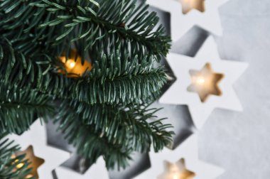 Sihirli Noel teması: rahat, sıcak ışıklar, çelenk, yıldızlar ve gri arkaplanda köknar dalları.