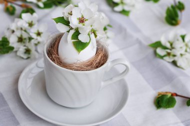 Güneşli bir günde, gri bir masa örtüsünün üzerinde beyaz bir yumurta içindeki doğal çiçeklerin parlak bahar Paskalya kompozisyonu..
