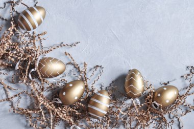 Altın renkli dekoratif Paskalya yumurtaları ve gri arka planda kağıt dekorları. Boşluğu kopyala
