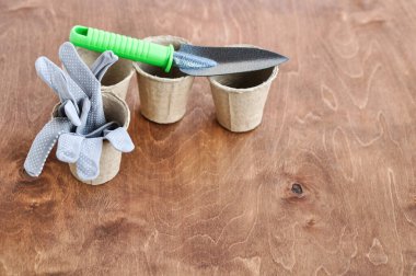 Tohumlar için turba kabında yeniden kullanılabilir gri bahçe eldivenleri ve kahverengi ahşap arka planda yanında metal bir kürek. Boşluğu kopyala