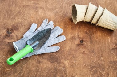 Bahçedeki fidanlar için bahar seti gri eldivenler, bir metal kürek ve kahverengi ahşap arka planda turba kapları. Düz yatıyordu