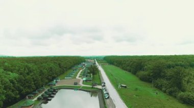 Flying over resort complex with same small houses, pool and pitch surrounded with green forest on both sides.