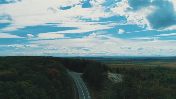 Aerial view of car driving along patched two lane road with dense woods growing both sides, with a car moving. — Stockvideo