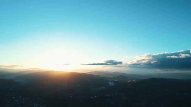 Vista aérea ascendente a través de suburbios poblados que albergan una amplia montaña silueta por el resplandor del amanecer en el horizonte . — Vídeo de stock