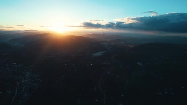 Rising aerial view across populated suburb housing to wide mountain silhouetted by sunrise glow on horizon. — Stok video