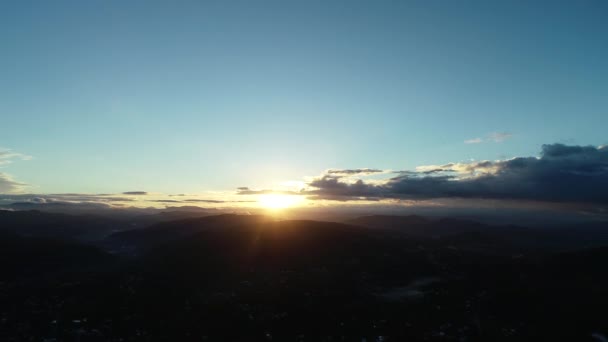 High altitude flight above populated landscape with misty silhouetted mountain range on horizon and view on sunset with fluffy clouds. — 비디오