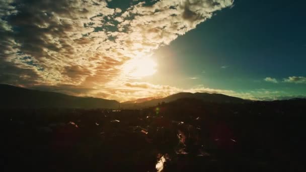 High altitude flight above populated landscape with misty silhouetted mountain range on horizon and view on sunset with fluffy clouds. — Stock videók