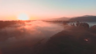 Scenic flight through the thick fog lying on fields and forests towards the sun.