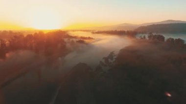 Scenic flight through the thick fog lying on fields and forests towards the sun.