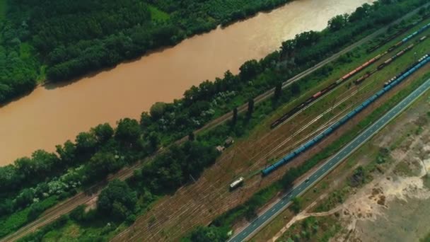 Vue de dessus sur de nombreuses voies ferrées et trains circulant le long d'une rivière à la campagne .