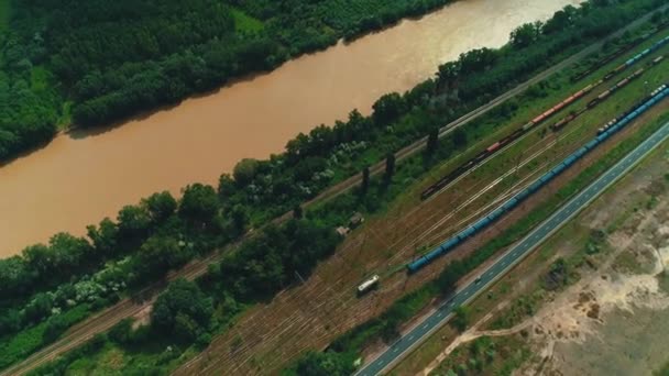 Вид сверху на многие железнодорожные пути и поезда, движущиеся вдоль реки в сельской местности . — стоковое видео