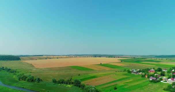 Vista aérea sobre pequeño pueblo con casas en verde valle de campos cultivados bajo cielo azul . — Vídeo de stock