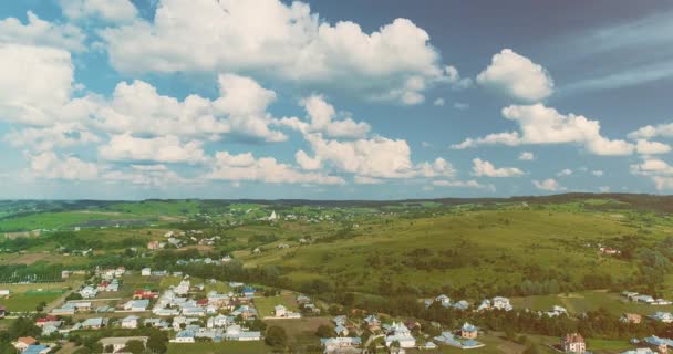 背景に美しい丘と曇り空の村の家の上にドローンが移動します。. — ストック動画