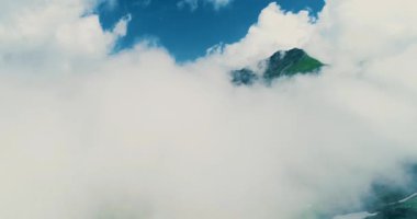 İHA mavi gökyüzünde uçuyor tüylü bulutların arasından gizemli dağların üzerinden gün ışığında..