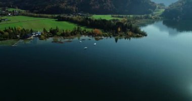 Görkemli dağlara tepeden bakan hava aracı ve berrak göl kıyısında tatil köyü..