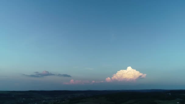 Różowo-pomarańczowa chmura w wieczornych promieniach słońca nad niebieskim wieczornym niebem z sylwetką gór na horyzoncie. — Wideo stockowe