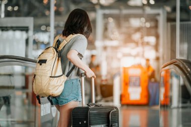 Modern havaalanı terminalinde bavulu çeken genç bir kadın. Taşıyıcıyı beklerken bavuluyla gezen adam. Dikiz aynası. Boşluğu Kopyala