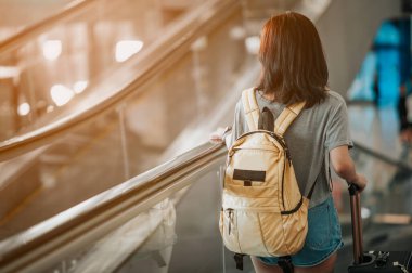 Modern havaalanı terminalinde bavulu çeken genç bir kadın. Taşıyıcıyı beklerken bavuluyla gezen adam. Dikiz aynası. Boşluğu Kopyala