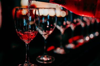 Barmen barda bir bardak şaraba şarap dolduruyor.